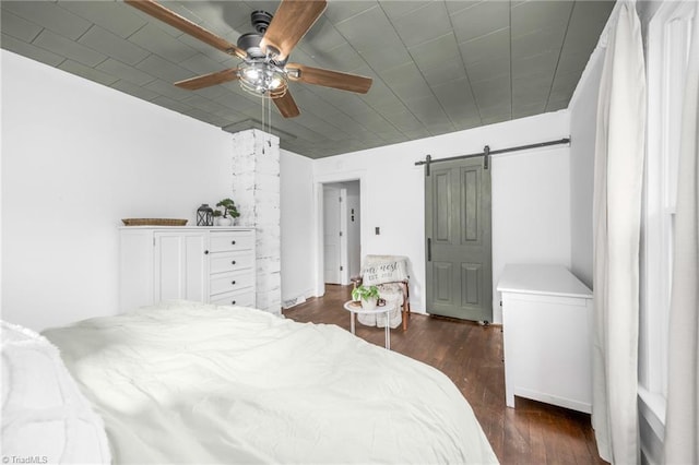 bedroom featuring a ceiling fan, dark wood finished floors, and a barn door