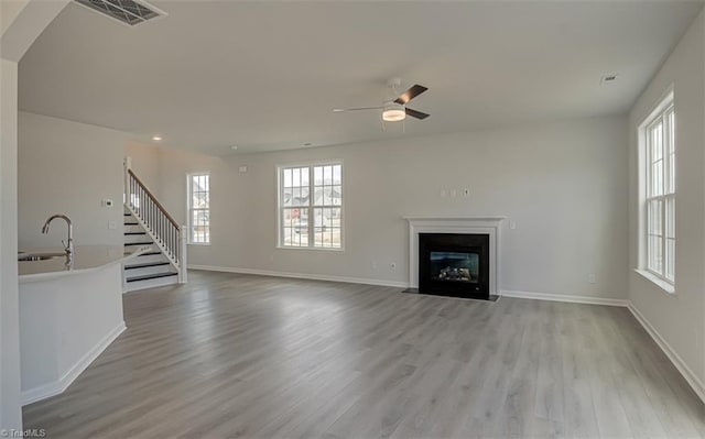 unfurnished living room with visible vents, a fireplace with flush hearth, a sink, light wood-type flooring, and stairs