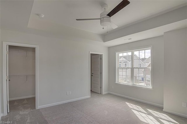 unfurnished bedroom featuring carpet floors, baseboards, a closet, a tray ceiling, and a walk in closet