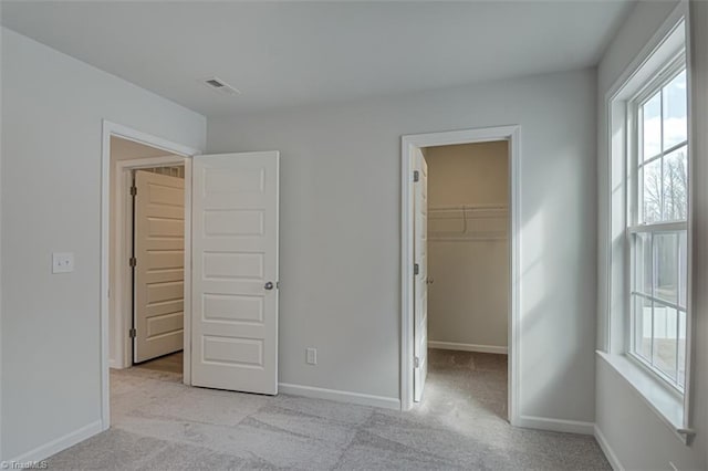 unfurnished bedroom featuring light carpet, visible vents, baseboards, and a walk in closet