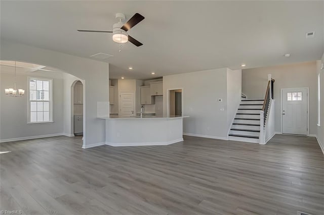 unfurnished living room with ceiling fan with notable chandelier, a sink, stairway, and wood finished floors