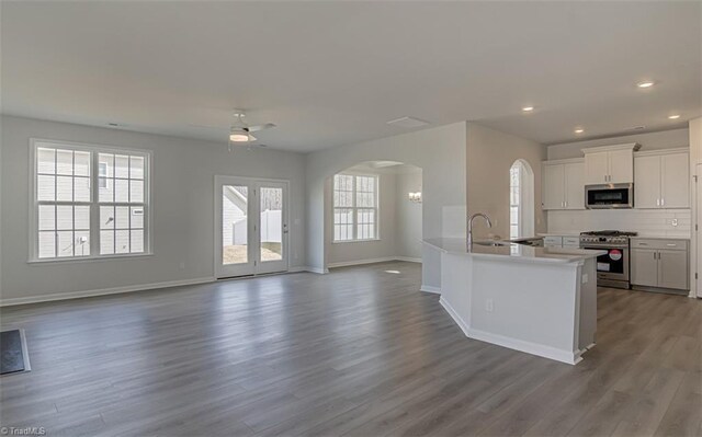 kitchen with arched walkways, white cabinets, open floor plan, appliances with stainless steel finishes, and dark wood finished floors