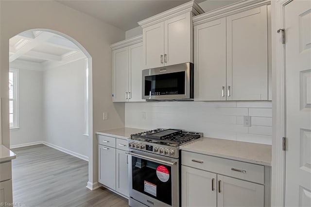 kitchen featuring tasteful backsplash, arched walkways, coffered ceiling, light wood-style flooring, and stainless steel appliances