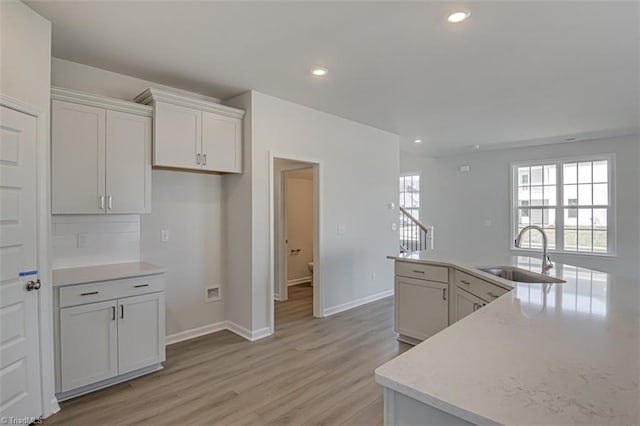 kitchen featuring recessed lighting, a sink, white cabinetry, baseboards, and light wood-style floors