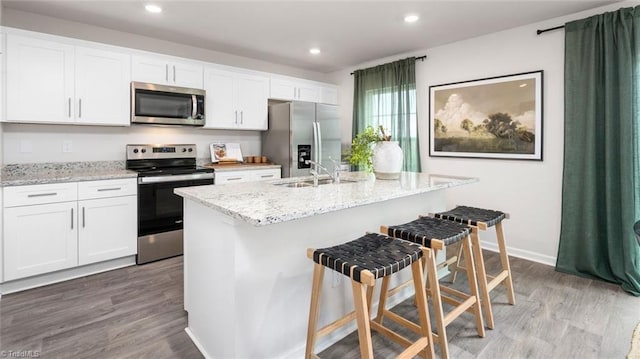 kitchen with sink, an island with sink, stainless steel appliances, light hardwood / wood-style floors, and white cabinets