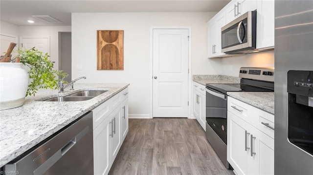 kitchen with appliances with stainless steel finishes, sink, white cabinets, light hardwood / wood-style floors, and light stone countertops