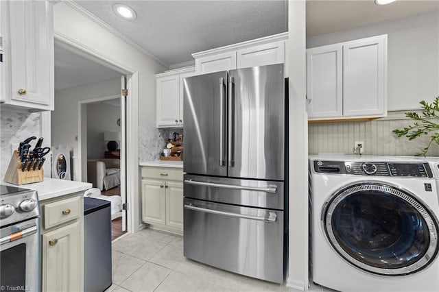 kitchen with light tile patterned floors, appliances with stainless steel finishes, white cabinetry, backsplash, and washer / dryer