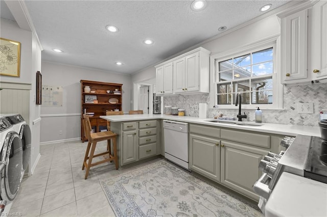 kitchen featuring kitchen peninsula, sink, a breakfast bar area, independent washer and dryer, and white dishwasher