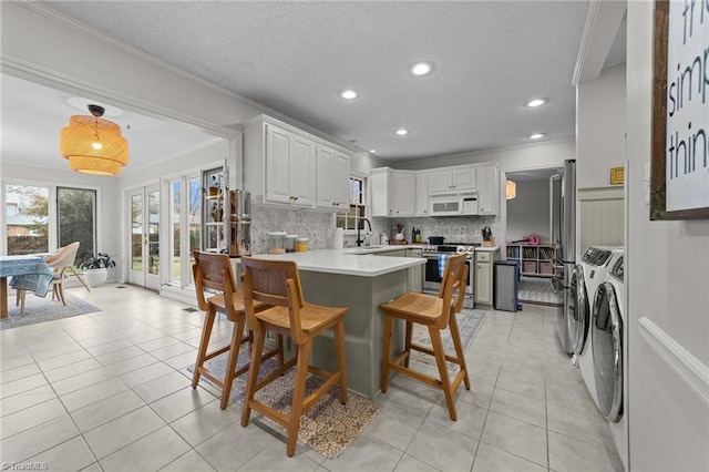 kitchen with sink, white cabinetry, kitchen peninsula, stainless steel stove, and washer and clothes dryer