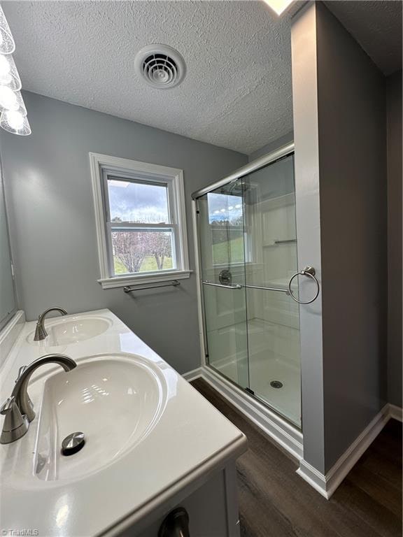 bathroom with a shower with shower door, wood-type flooring, a textured ceiling, and vanity