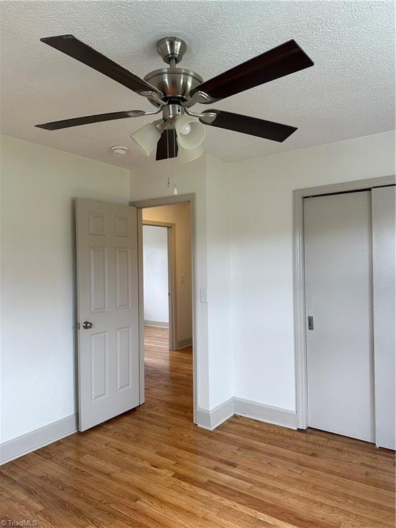 unfurnished bedroom with ceiling fan, a closet, a textured ceiling, and light wood-type flooring