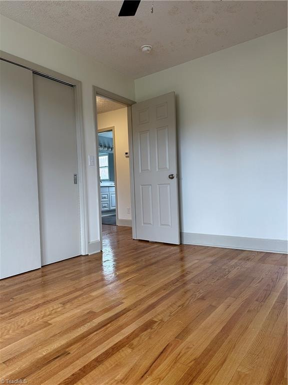 unfurnished bedroom with a textured ceiling, a closet, light hardwood / wood-style flooring, and ceiling fan