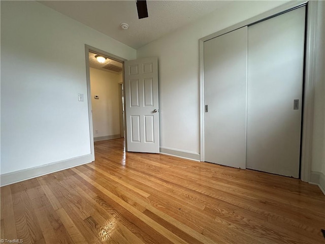 unfurnished bedroom with ceiling fan, light hardwood / wood-style floors, a textured ceiling, and a closet