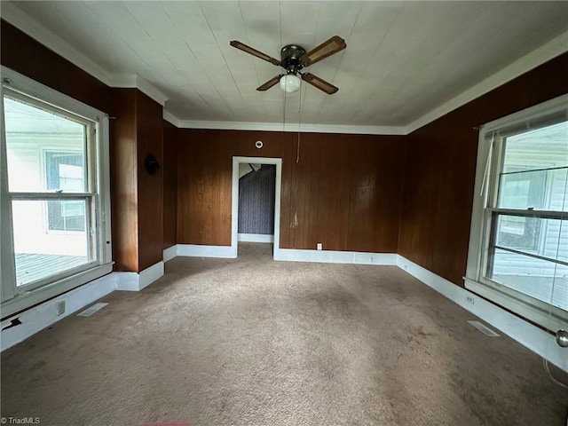 unfurnished room with ceiling fan, wooden walls, ornamental molding, and carpet