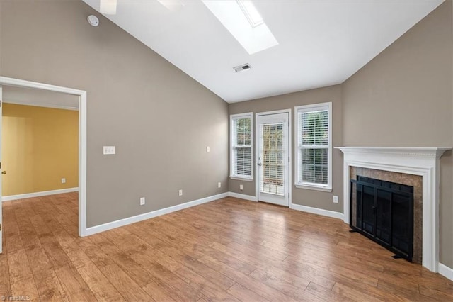 unfurnished living room with high vaulted ceiling, a skylight, light hardwood / wood-style flooring, ceiling fan, and a tiled fireplace