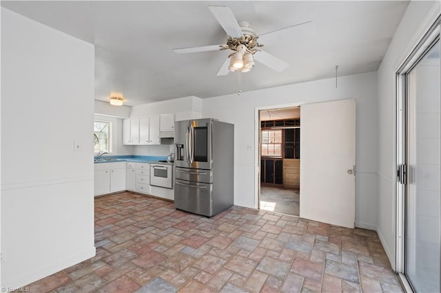 kitchen featuring ceiling fan, white stove, sink, white cabinets, and stainless steel fridge