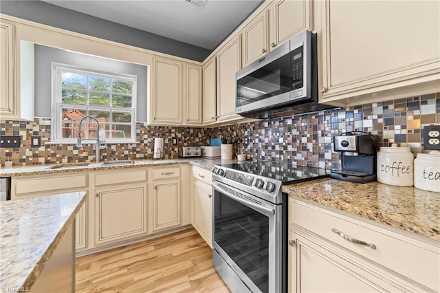 6416 Rock Springs Rd, Greensboro, NC 27410 - kitchen with appliances with stainless steel finishes, cream cabinetry, light wood-style flooring, and decorative backsplash