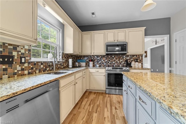 6416 Rock Springs Rd, Greensboro, NC 27410 - kitchen featuring appliances with stainless steel finishes, cream cabinets, light wood-style floors, light stone counters, and tasteful backsplash