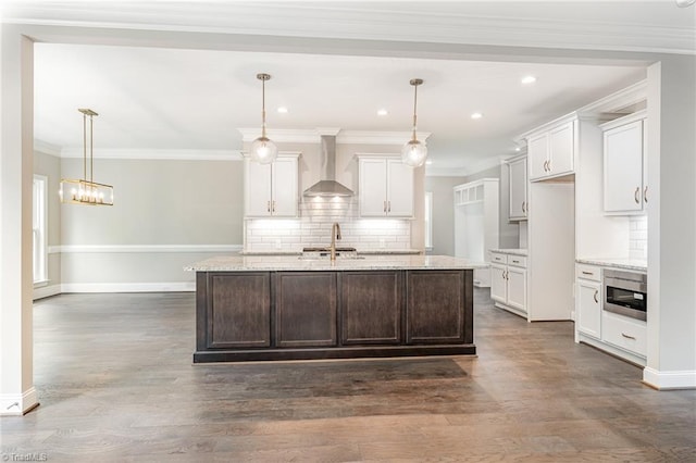 kitchen with dark wood-style flooring, white cabinets, crown molding, and wall chimney range hood