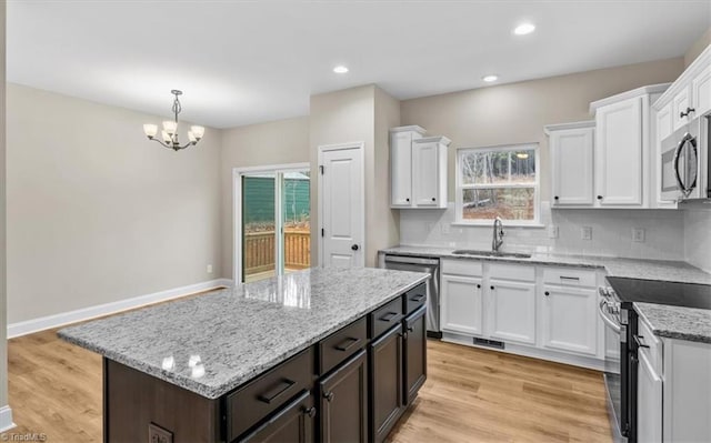 kitchen featuring sink, white cabinetry, stainless steel appliances, a kitchen island, and decorative light fixtures