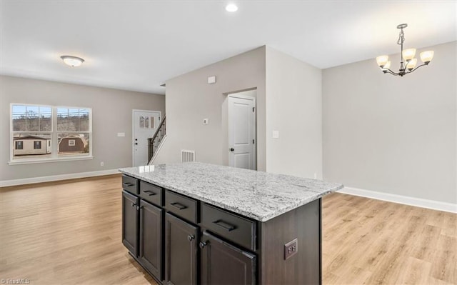 kitchen with pendant lighting, dark brown cabinets, a kitchen island, and light hardwood / wood-style flooring