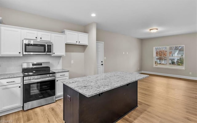 kitchen with white cabinetry, a center island, light hardwood / wood-style flooring, stainless steel appliances, and light stone countertops