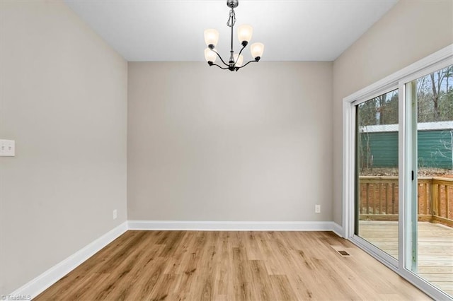 spare room with a notable chandelier and light wood-type flooring