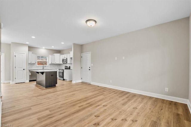 kitchen with a kitchen island, a breakfast bar, white cabinetry, stainless steel appliances, and light hardwood / wood-style flooring