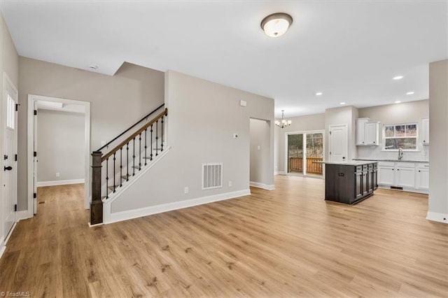 unfurnished living room featuring an inviting chandelier, sink, and light hardwood / wood-style floors