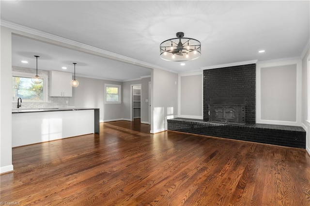 unfurnished living room featuring a brick fireplace, dark wood-style flooring, a healthy amount of sunlight, and crown molding