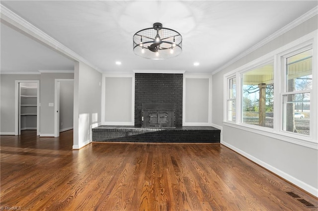 unfurnished living room with wood finished floors, visible vents, baseboards, a brick fireplace, and crown molding