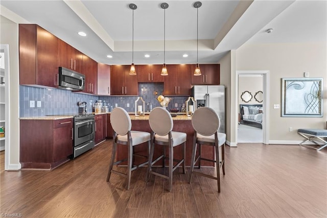 kitchen with appliances with stainless steel finishes, dark hardwood / wood-style flooring, decorative light fixtures, and light stone counters