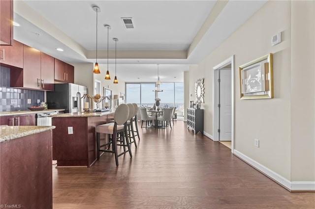 kitchen featuring light stone countertops, dark hardwood / wood-style floors, stainless steel fridge, a kitchen bar, and a center island with sink