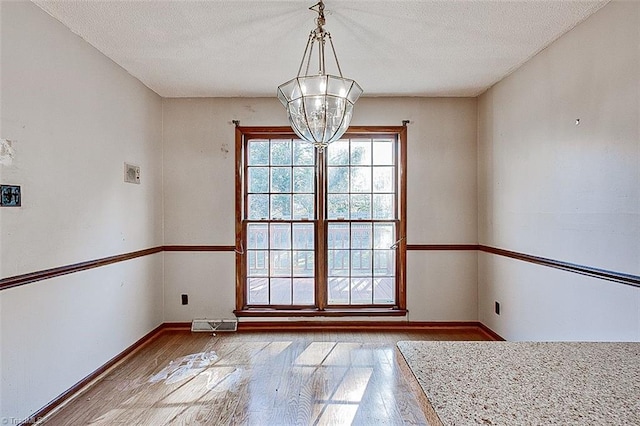 unfurnished dining area featuring visible vents, a notable chandelier, a textured ceiling, hardwood / wood-style floors, and baseboards