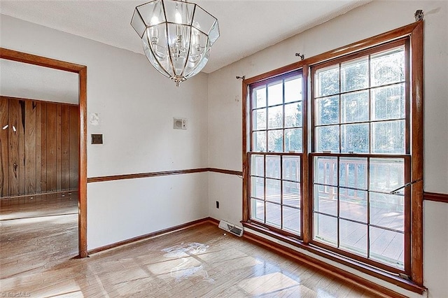 empty room featuring wooden walls, visible vents, baseboards, and an inviting chandelier