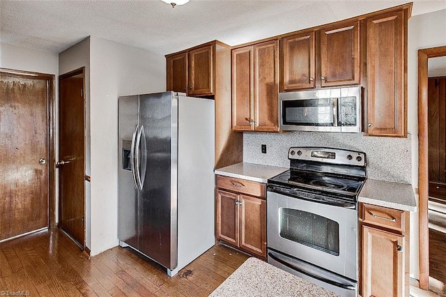 kitchen featuring backsplash, a textured ceiling, appliances with stainless steel finishes, light countertops, and dark wood-style flooring