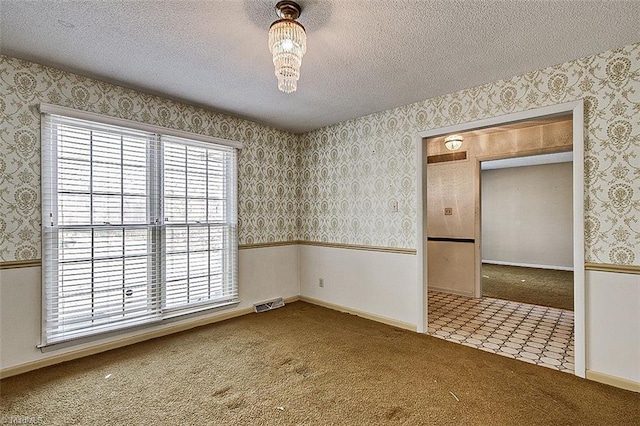 empty room with wallpapered walls, wainscoting, carpet floors, and a textured ceiling