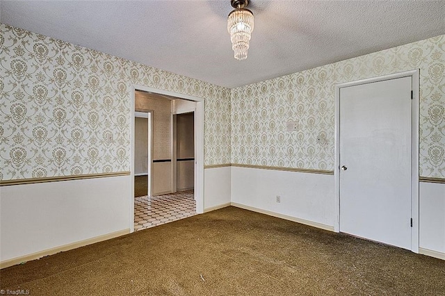 unfurnished room featuring a wainscoted wall, carpet flooring, a textured ceiling, and wallpapered walls