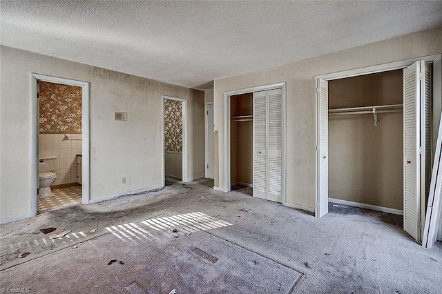 unfurnished bedroom with tile walls, ensuite bathroom, two closets, and a textured ceiling