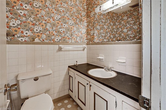 half bath with wainscoting, wallpapered walls, vanity, and toilet