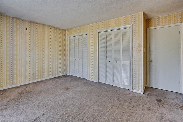 unfurnished bedroom featuring wallpapered walls, two closets, carpet floors, and a textured ceiling