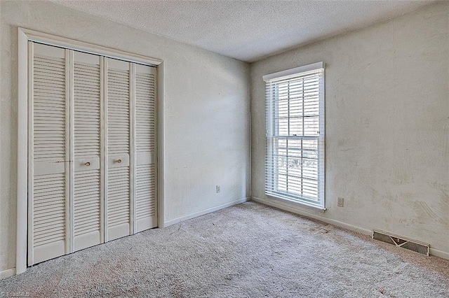 unfurnished bedroom featuring visible vents, a textured ceiling, a closet, carpet flooring, and baseboards