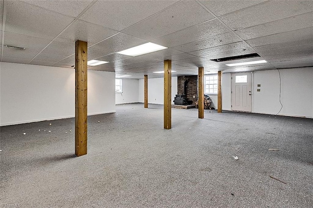 below grade area with a paneled ceiling, baseboards, and a wood stove