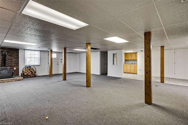 basement featuring a paneled ceiling, a wood stove, and carpet