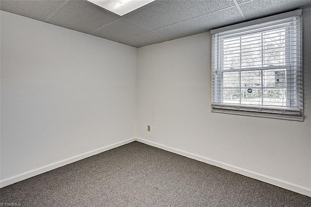 unfurnished room with a paneled ceiling, baseboards, and dark carpet