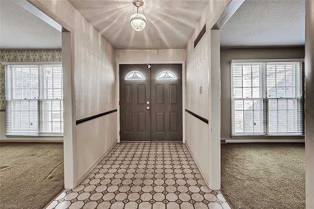 carpeted entrance foyer featuring tile patterned floors, plenty of natural light, wallpapered walls, and a textured ceiling