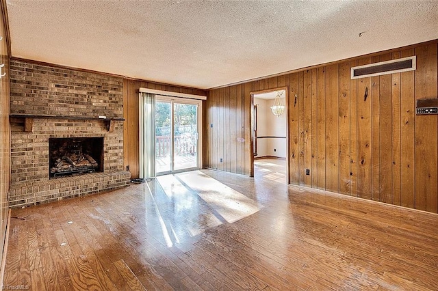 unfurnished living room featuring visible vents, wood walls, a fireplace, a textured ceiling, and wood-type flooring