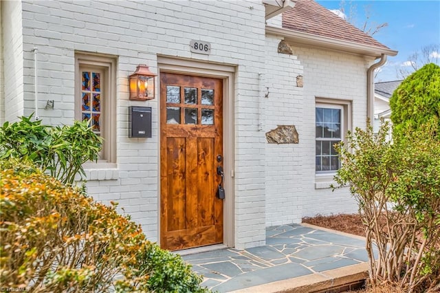 doorway to property featuring brick siding and a shingled roof