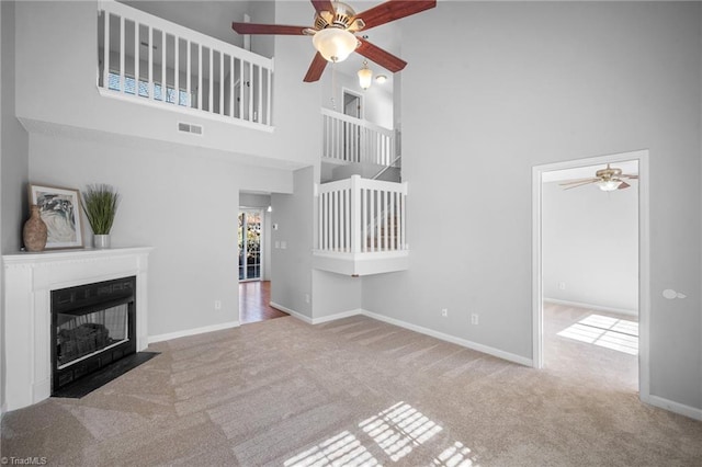 unfurnished living room with ceiling fan, light colored carpet, and a high ceiling