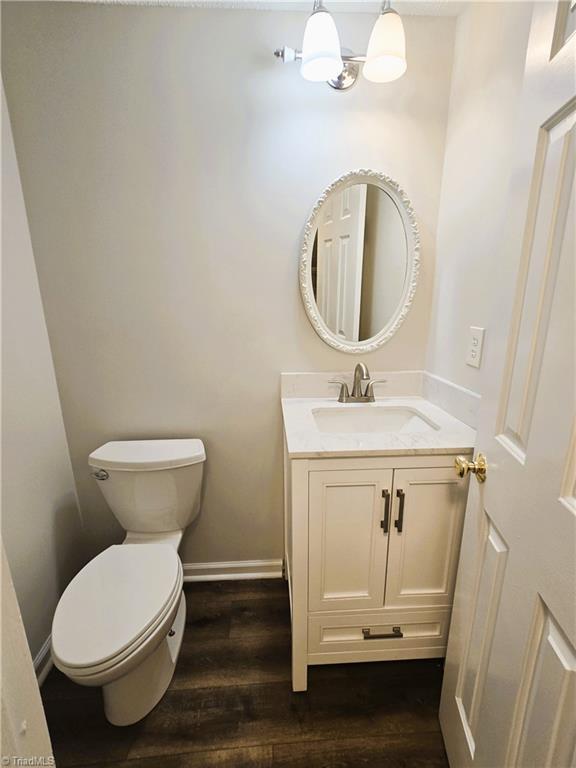 bathroom with wood-type flooring, an inviting chandelier, toilet, and vanity